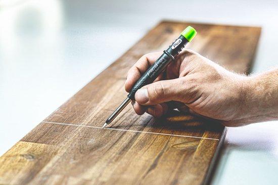 Hand houdt Pica-Dry markeerstift met groene dop om te schrijven op een houten oppervlak.