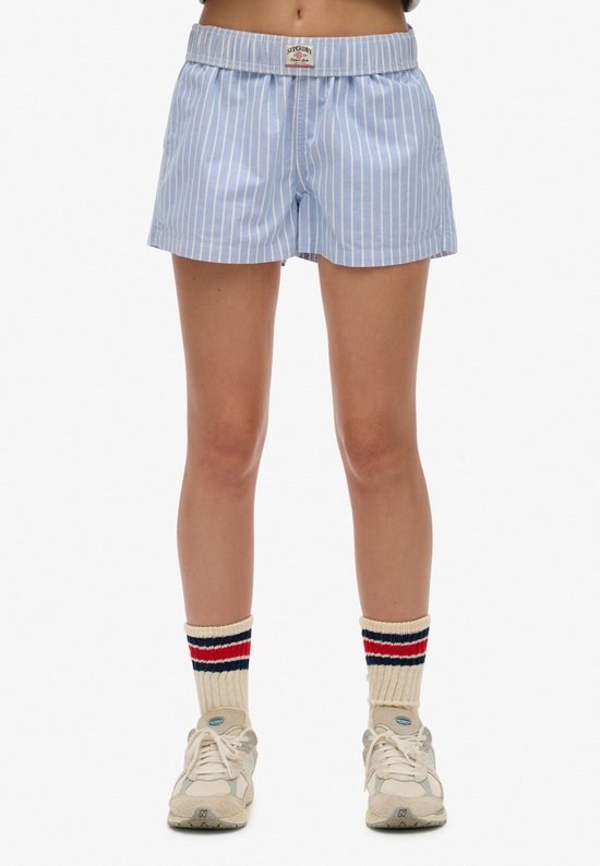 Bas du corps d'un mannequin portant un short bleu clair à rayures verticales blanches, des chaussettes et des baskets.