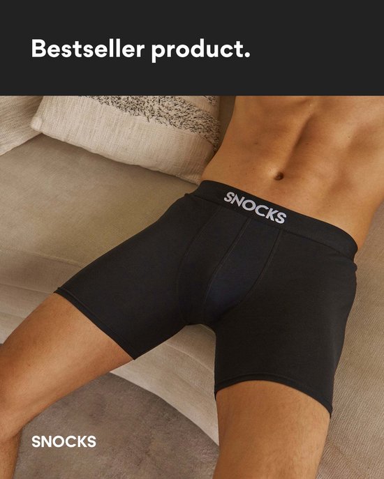 Man ligt op een bank, draagt korte zwarte SNOCKS boxershorts met logo op de tailleband.