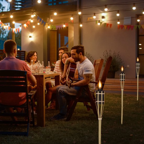 Een groep vrienden geniet van een diner in de tuin bij kaarslicht van bamboe fakkels.