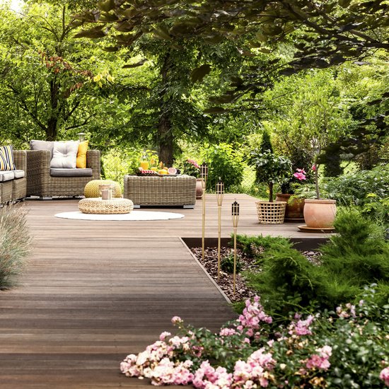 Luxe houten terras met tuinmeubelen, plantenbakken en brandende bamboe tuinfakkels.