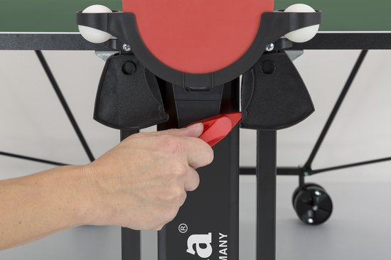 Een hand pakt een rood object op de houder van een tafeltennisbatje aan de zijkant van de tafel.