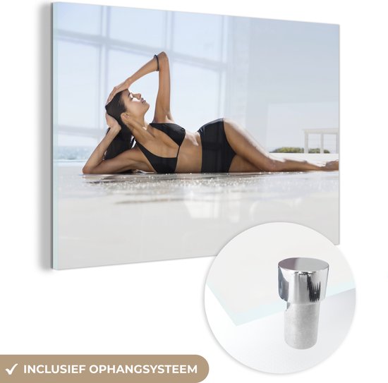 MuchoWow® Glasschilderij 90x60 cm - Schilderij acrylglas - Een vrouw in een zwarte bikini poseert op het strand - Foto op glas - Schilderijen