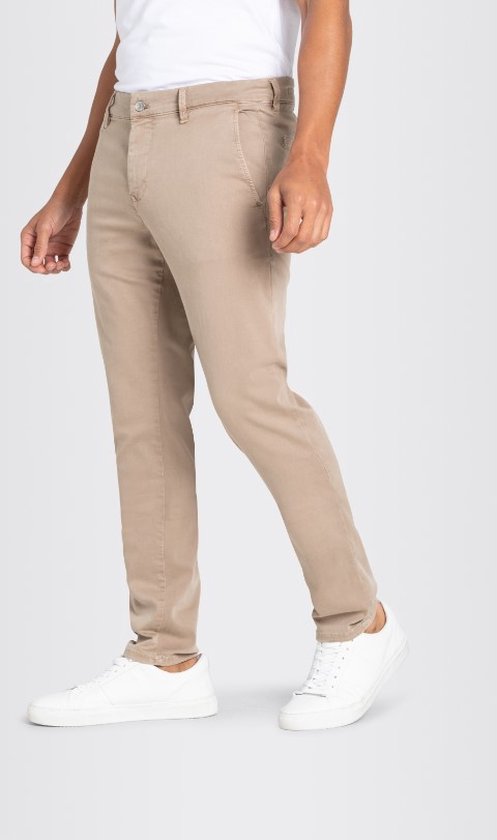 Man in beige chino broek met witte T-shirt en witte sneakers, handen in zakken.