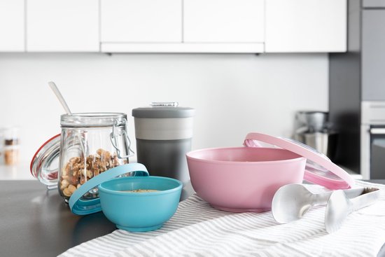 Un bol rose et bleu, une tasse grise, un bocal en verre avec des noix et des ustensiles de cuisine sur un comptoir.