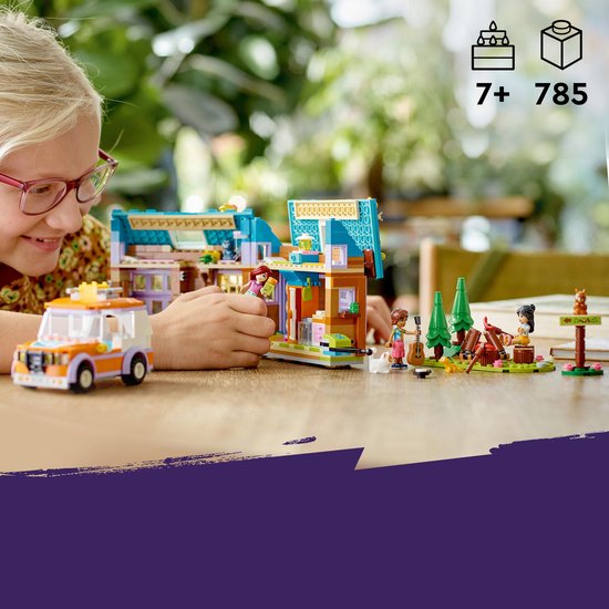 Kind bouwt een LEGO Friends kampeer set met huisje, auto, poppetjes, dieren en campfire op een tafel.