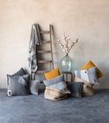 Collectie van grijze, gele en blauwe kussens en plaids, gerangschikt op een ladder en in manden.