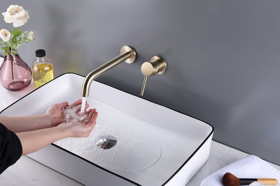 Handen die water opvangen onder een gouden wandkraan boven een witte wastafel met zwarte rand.