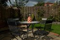 Terracotta kaarsenwarmer op een tuintafel met stoelen en achtergrond van een schutting.