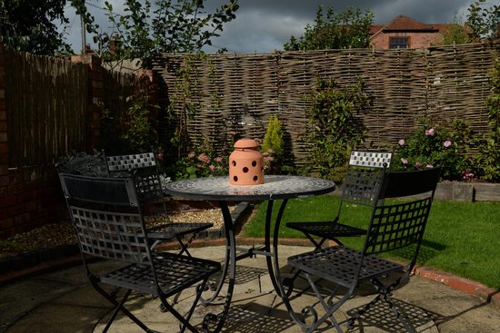 Terracotta kaarsenwarmer op een tuintafel met stoelen en achtergrond van een schutting.