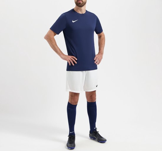 Model in compleet sporttenue: donkerblauw Nike sportshirt, witte korte broek, marineblauwe sokken.