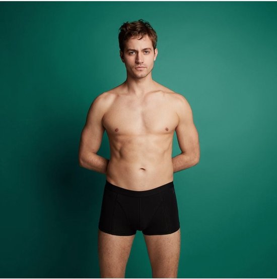 Model draagt een zwarte Ten Cate shorty tegen een groene achtergrond.