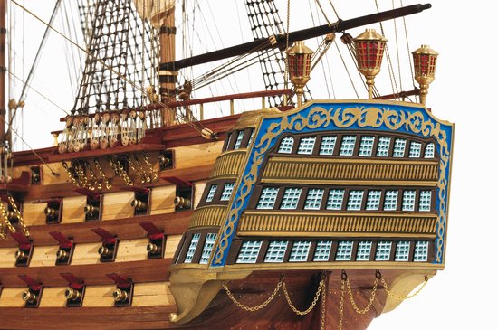 Boeg van een houten modelschip met gouden versieringen en blauwe ramen.