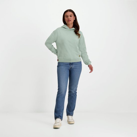 Model draagt een mintgroene NOMAD hoodie met klein geel logo en jeans.