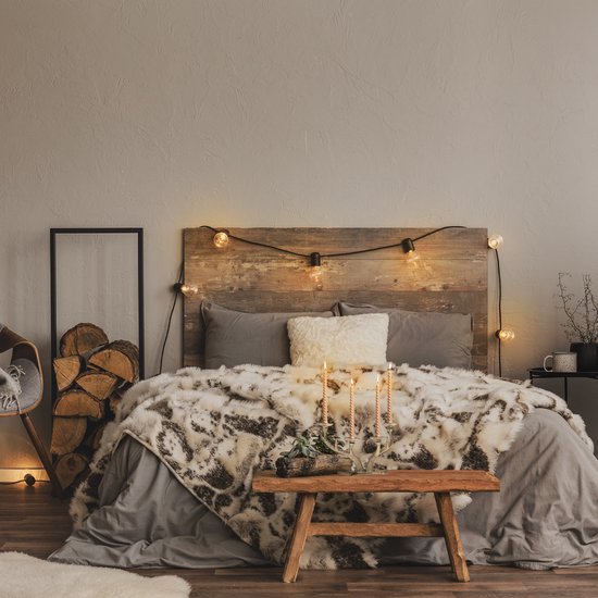 Gouden gewei kandelaar met drie beige kaarsen op een houten bijzettafeltje in een slaapkamer.