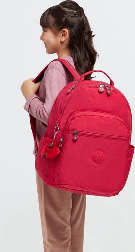 Une fille portant un sac à dos sur ses épaules, vue de dos, avec un sac à dos Kipling rouge.