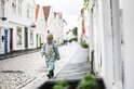 Jongen in groen gestreept regenpak loopt op geplaveide straat in een stadje.