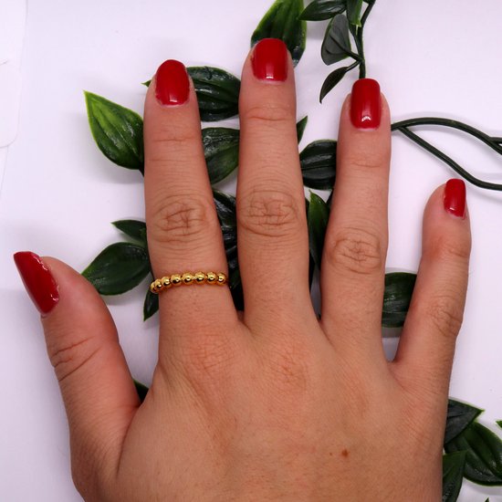 Gouden ring met balletjes, gedragen op de middelvinger van een hand met rode nagellak.