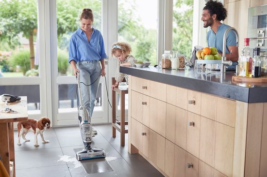 Vrouw in blauw shirt en spijkerbroek maakt de vloer schoon met een Bissell Crosswave C3 Select steelstofzuiger.