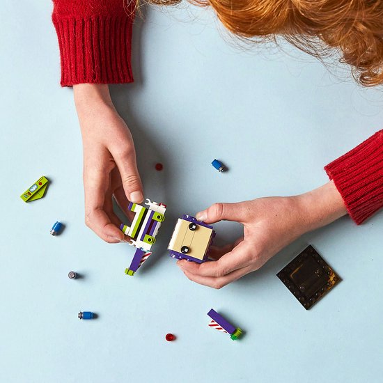 Twee handen bouwen aan een LEGO BrickHeadz Buzz Lightyear met paarse, witte en groene steentjes.