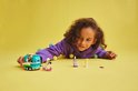 Kind liggend op een gele achtergrond met een LEGO Friends mobiele bubbelthee stand, twee poppen en een scooter.