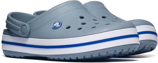 Een paar grijze Crocs clogs met een witte en blauwe streep op de zool, op de voorgrond.