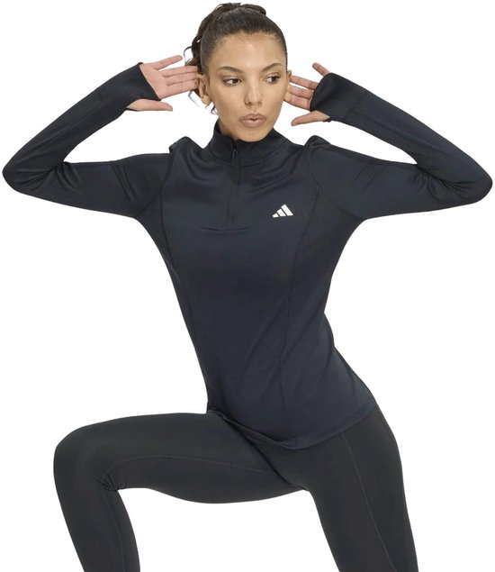 Model in een dynamische pose, draagt een zwart Adidas sportshirt met halve rits.