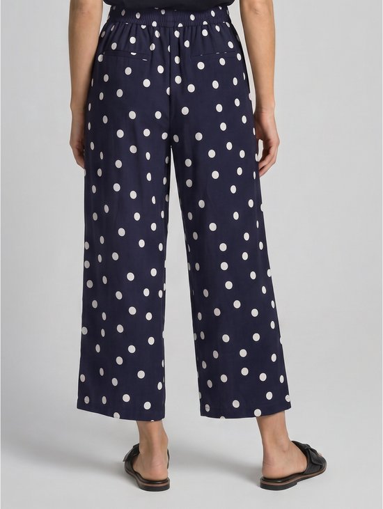 Achterkant van een model in een marineblauwe culotte met witte polkadotprint, wijde pijpen en hoge taille.