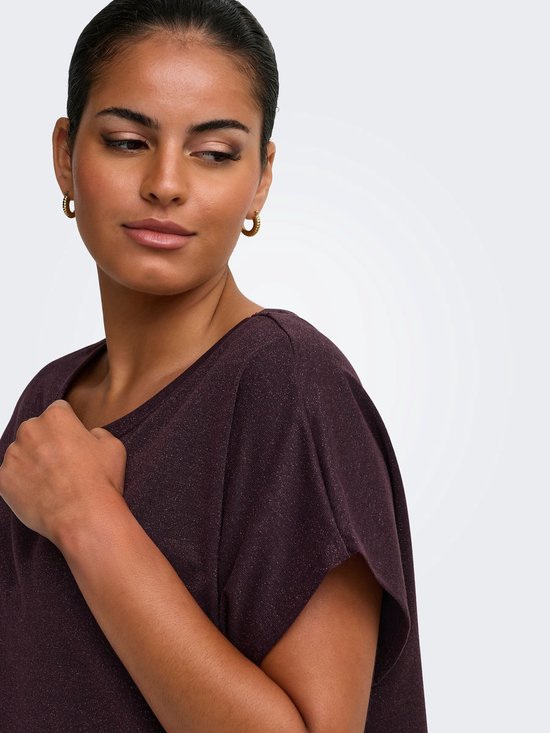 Close-up van het gezicht van een model dat wegkijkt, met een hand op haar borst, in een donkerpaarse glittertop.