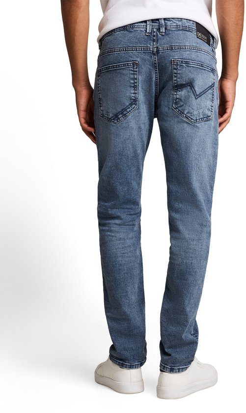 Model met de rug naar de camera, draagt blauwe jeans met lichte wassing, zakken met stiksels.