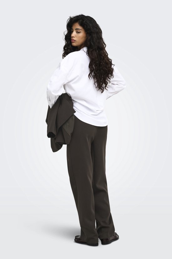 Model van achteren gezien in een wit overhemd en donkerbruine pantalon, met jas over de arm.