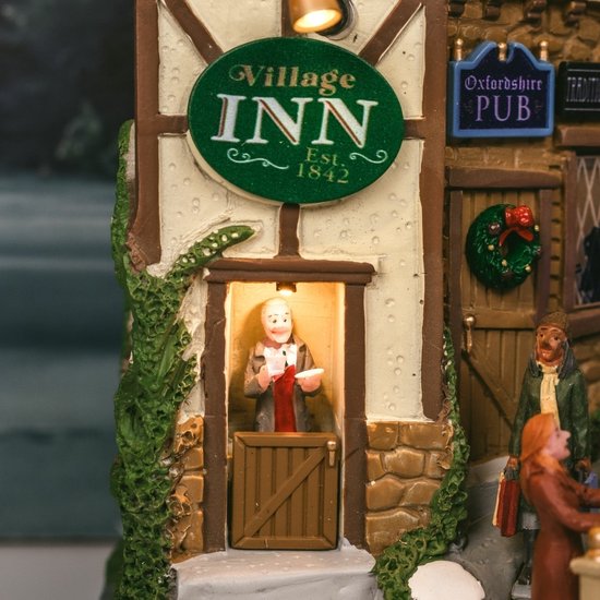 Close-up van de 'Village Inn' gevel met een verlichte barman achter een houten deur.