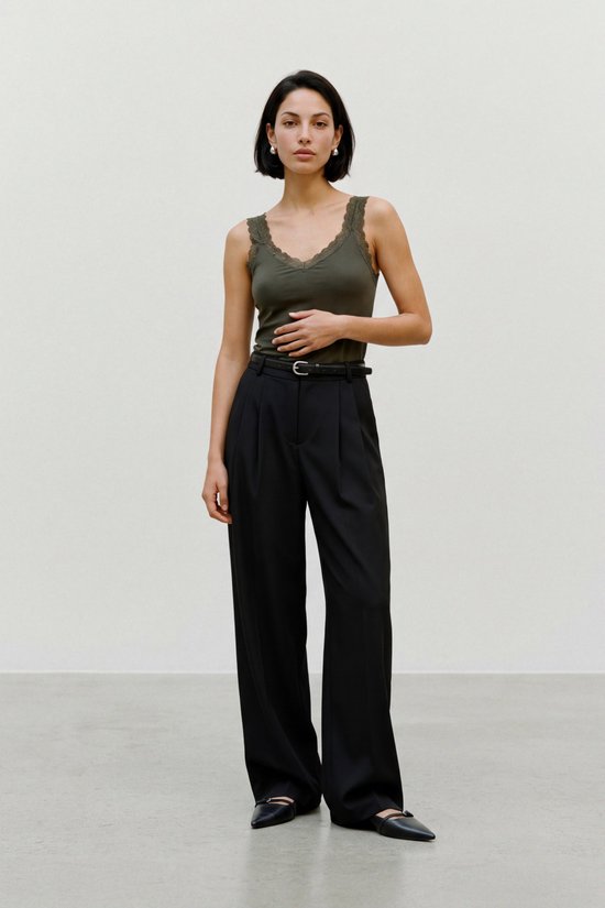 Model in een olijfgroene VERO MODA singlet met kanten halslijn, zwarte pantalon en zwarte ballerina's.