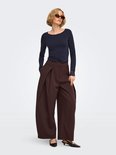 Model met zonnebril draagt een bruine wijde broek met plooien en een donkerblauw shirt met kanten details.