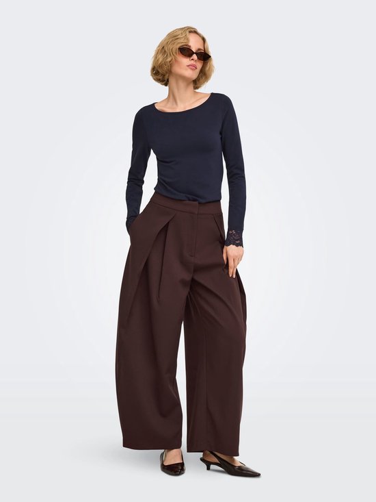 Model met zonnebril draagt een bruine wijde broek met plooien en een donkerblauw shirt met kanten details.