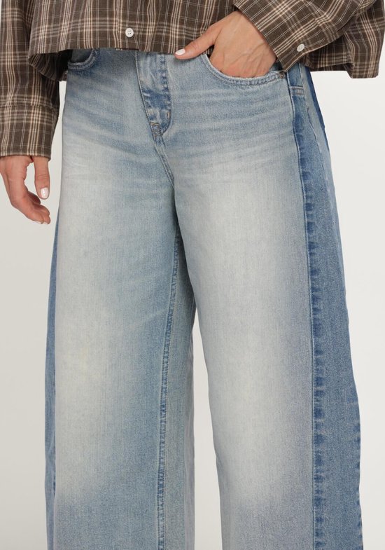 Close-up van de taille en heupen van een wijde jeans met zijpanelen in een donkerdere blauwtint.