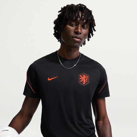 Model draagt een zwart sportshirt met oranje Nike logo op de borst en Nederlands elftal logo.