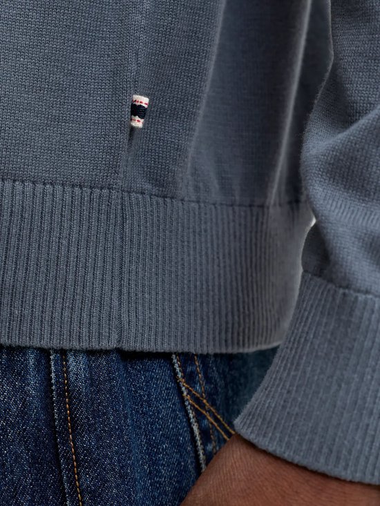 Detail van de onderkant van een donkerblauwe gebreide poloshirt met een klein label.