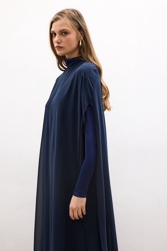 Model in een donkerblauwe jurk met hoge hals en wijde, doorschijnende chiffon mouwen over een nauwsluitende, lange mouw.