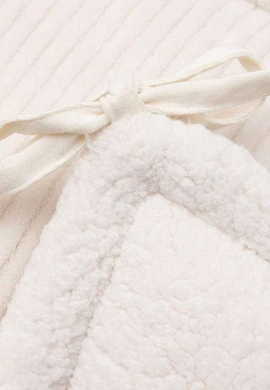 Detail van een crèmekleurige bedbumper met zachte teddy stof aan één zijde en ribstof aan de andere. Vastgebonden met een lint.