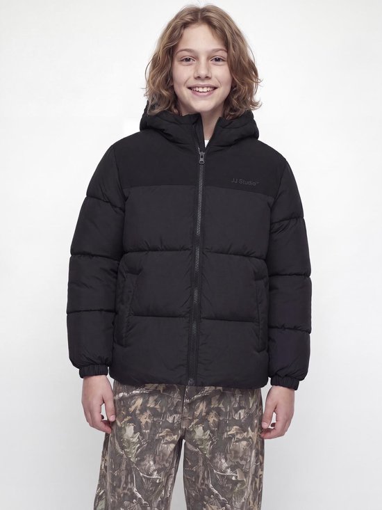 Jongen draagt een zwarte JJ Studio gewatteerde jas met capuchon en camouflagebroek.