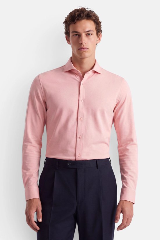 Model draagt een roze piqué katoenen overhemd en een donkerblauwe pantalon.