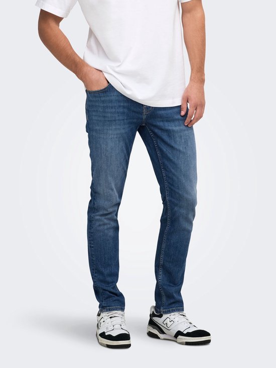Model draagt een donkerblauwe slim-fit jeans met een wit T-shirt en zwart-witte sneakers.
