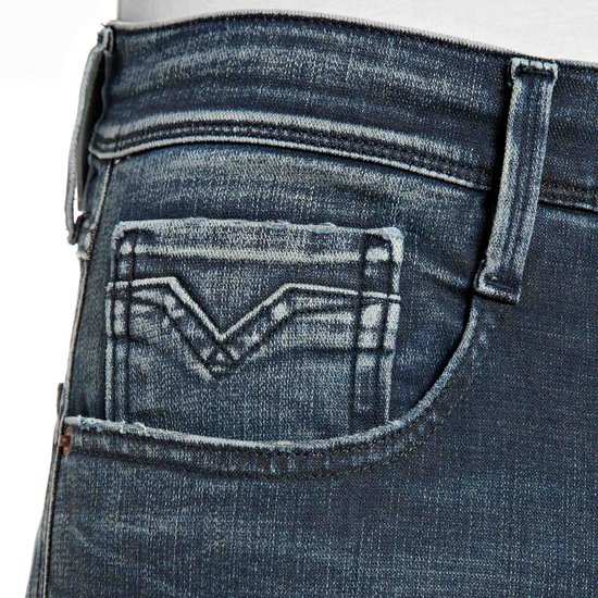 Close-up van de voorzak van een donkerblauwe Replay jeans met V-vormige stiksels.