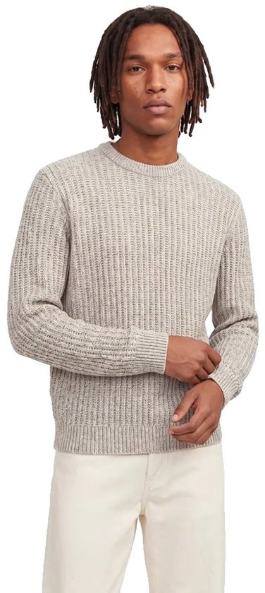 Model met dreadlocks draagt een beige trui en een witte broek.