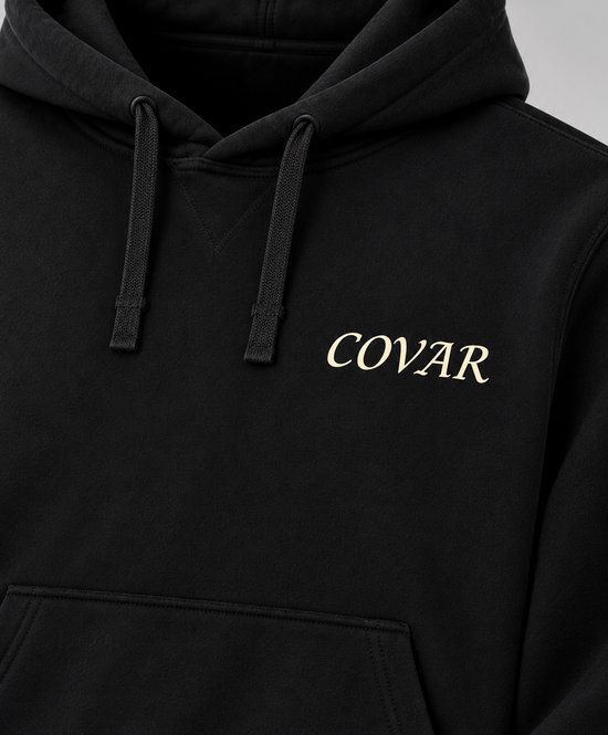 Detail van een zwarte hoodie met het crèmekleurige COVAR-logo en de kangoeroezak.