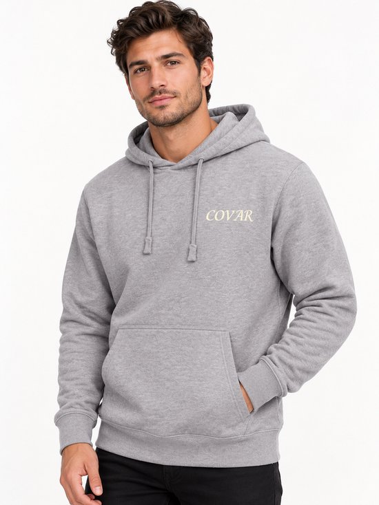 Man met grijze hoodie met 'COVAR' print op linkerborst. Hand in zak.