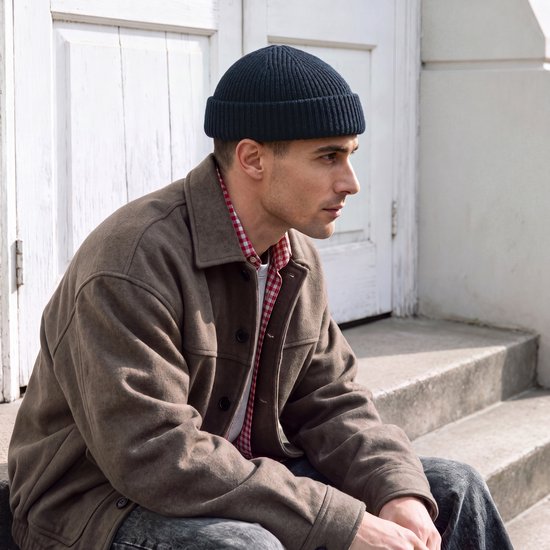 Man met donkerblauwe beanie, bruine jas en geruite blouse.