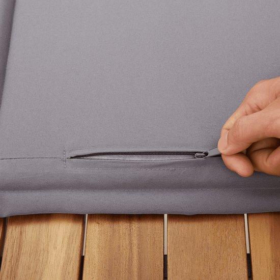Main ouvrant la fermeture éclair d'un coussin d'extérieur gris au-dessus d'une surface en bois.