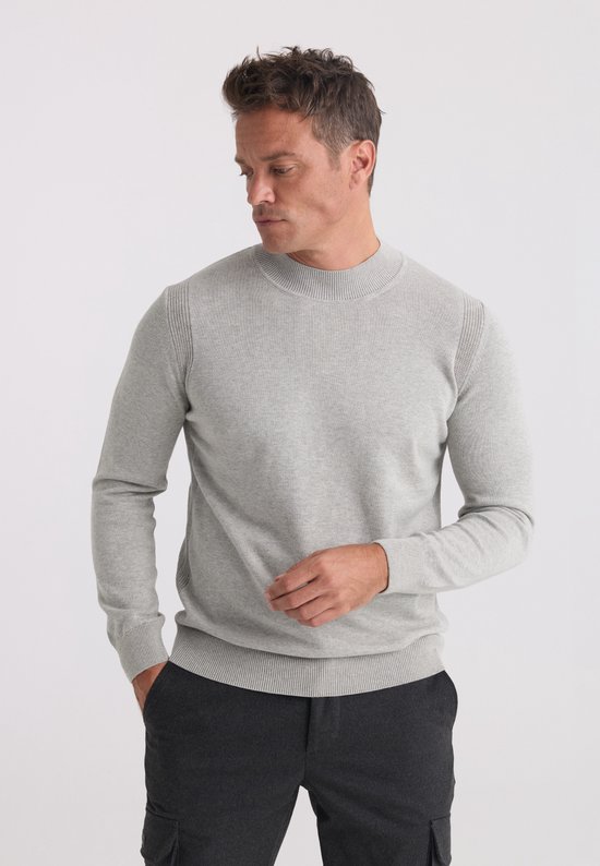 Model draagt een grijze gebreide trui met opstaande kraag en textuurdetails op de schouders.